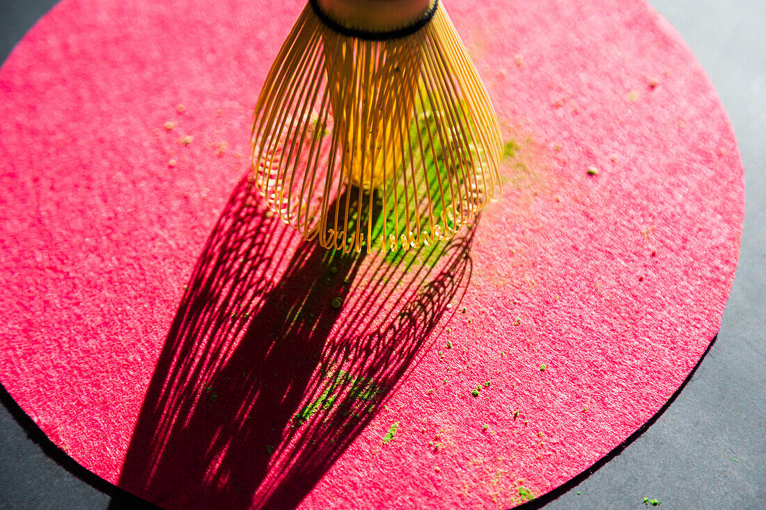 Bamboo chasen und pulverisierte getrocknete Matcha auf rosa Kreis auf schwarzem Tisch im Sonnenlicht