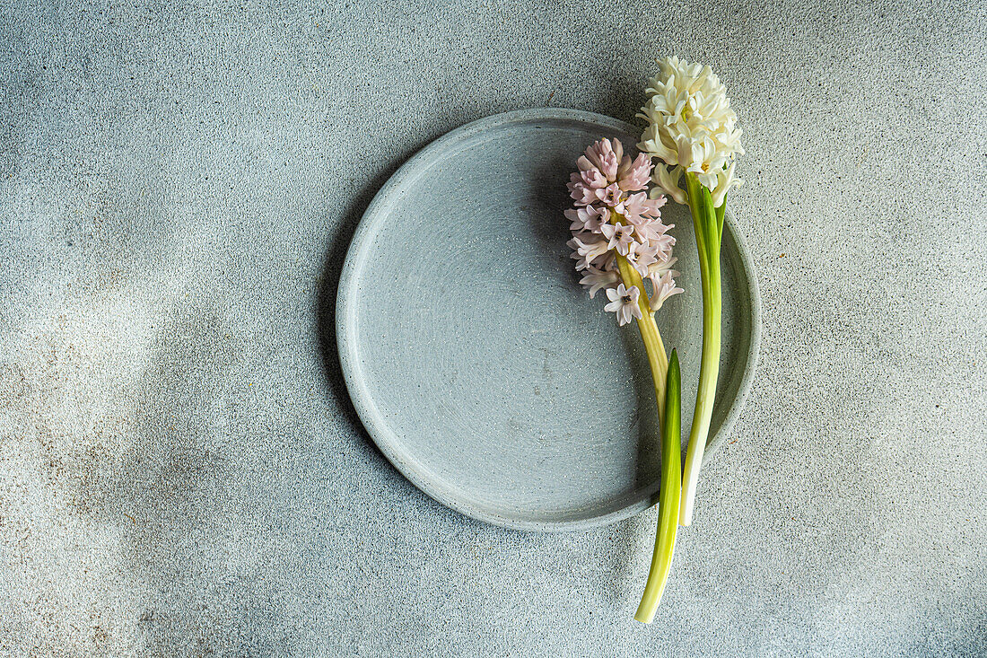 From above spring table setting with hyacinth flower near ceramic plate on grey concrete table for festive dinner