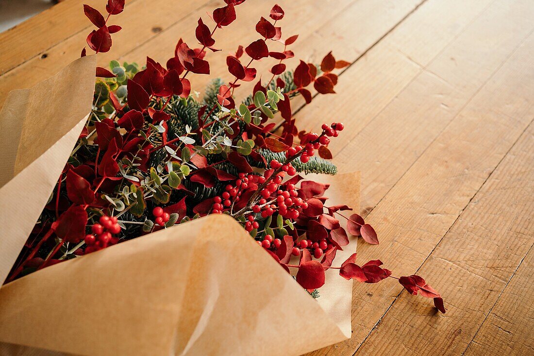 From above of festive stylish decorative Christmas bouquet with twigs of eucalyptus and bright red branches with berries placed on wooden table in room