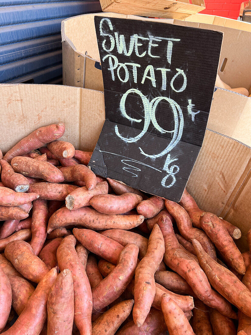 Rohe Süßkartoffeln in einer Kartonschachtel an einem Stand auf einem lokalen Markt von oben