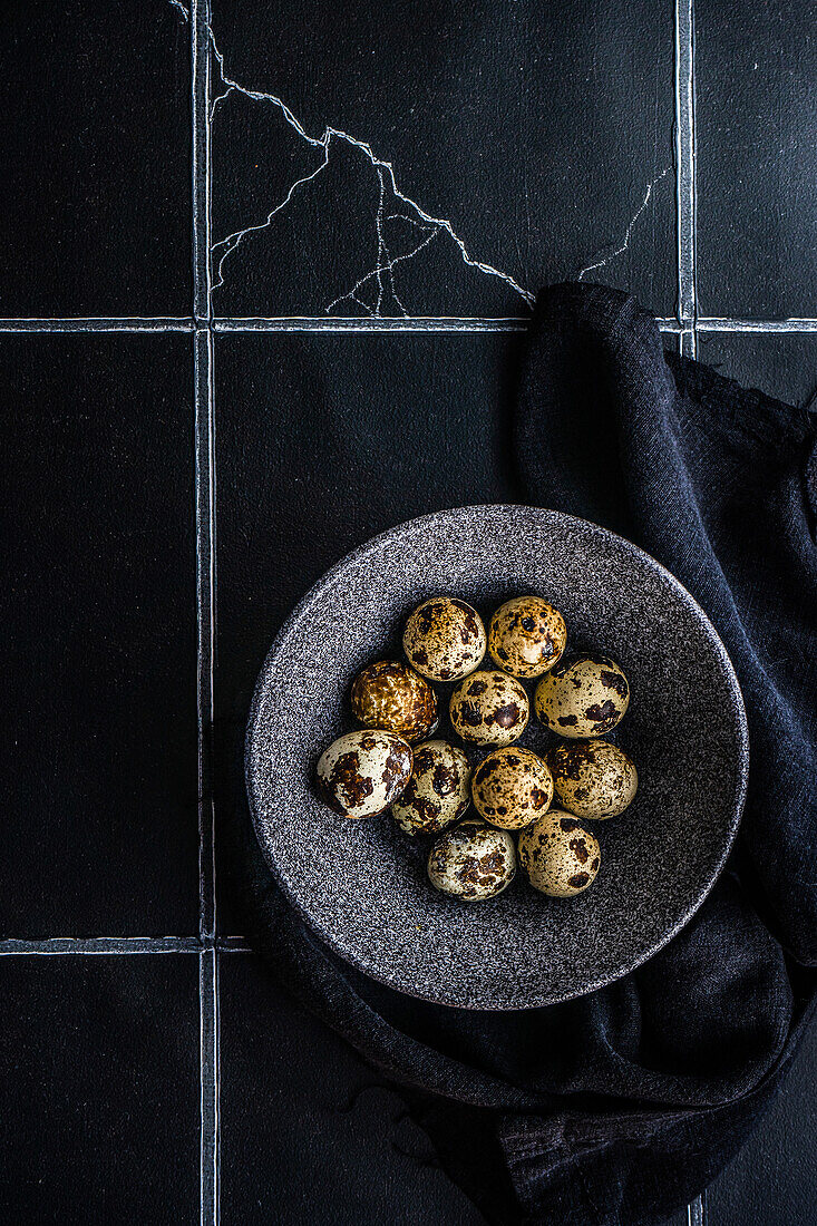 From above ceramic bowl with raw quail eggs on tiled table
