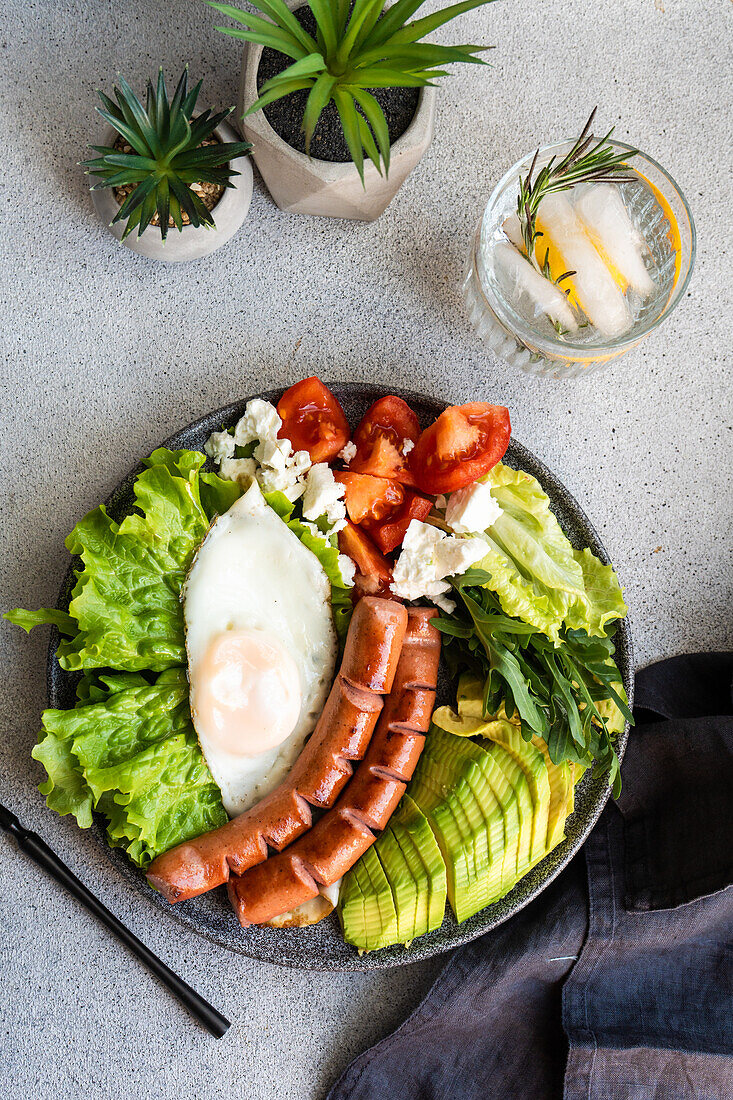 healthy ketogenic lunch plate with vegetables, fried egg and sausages served on the concrete plate