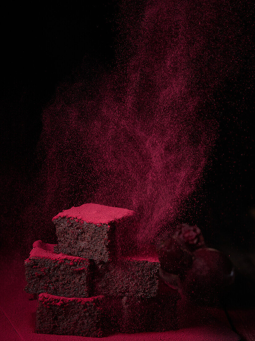 Puderzucker auf einem Haufen leckerer, frisch gebackener Brownie-Scheiben auf einem Tisch in einem dunklen Studio vor schwarzem Hintergrund