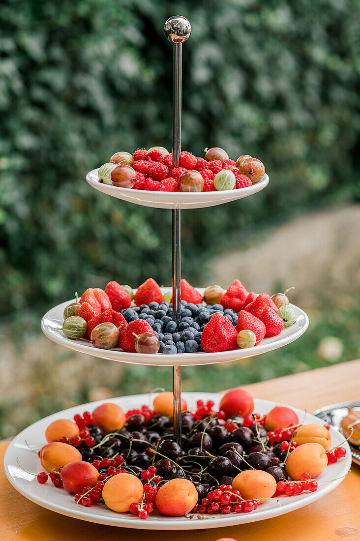Köstliche reife Beeren und Früchte, serviert auf einer dreistöckigen Platte auf einem Tisch während eines Banketts im Freien
