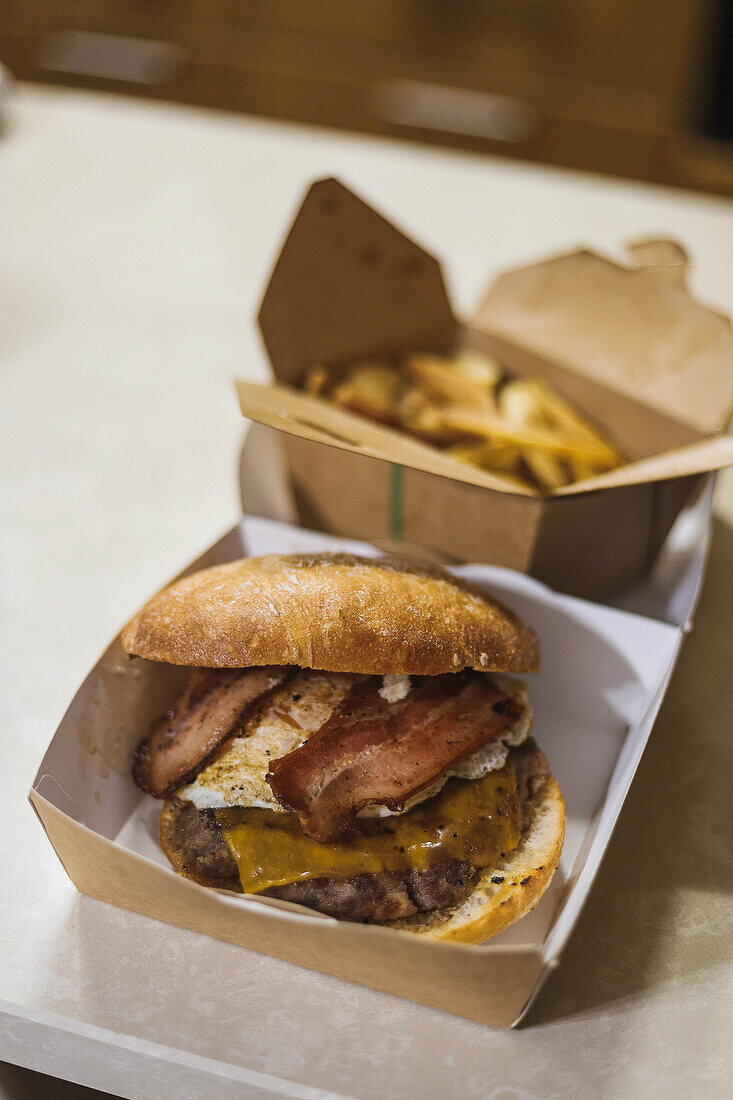 High angle of appetizing hamburger with bacon and crispy potato wedges served on table in carton packages