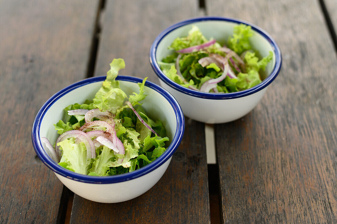High angle of bowls with salad leaves and onion sprinkled with seasoning placed on wooden table