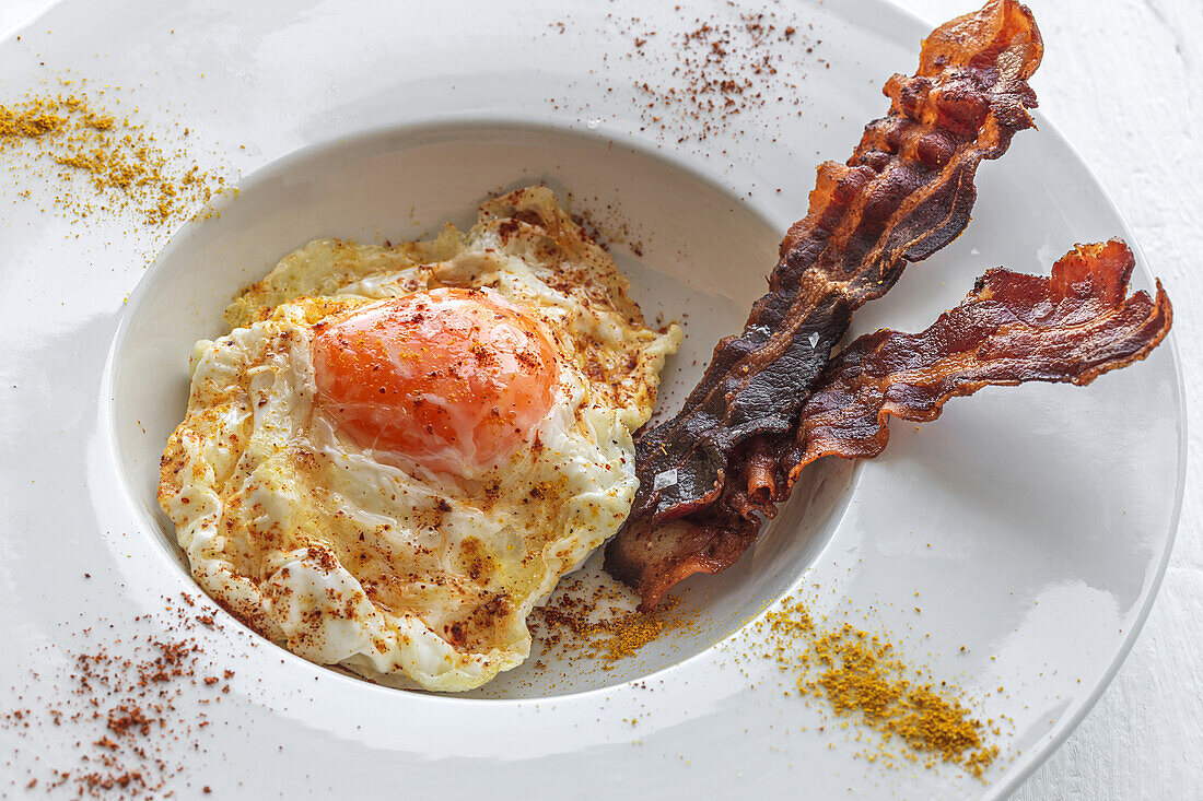 Overhead view of tasty eggs with fried bacon strips on plate