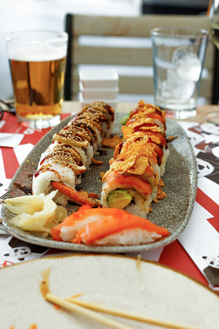 Hoher Winkel von appetitlichem Murakami-Sushi mit Stäbchen und einem Glas Bier auf einem Tisch in einem Restaurant