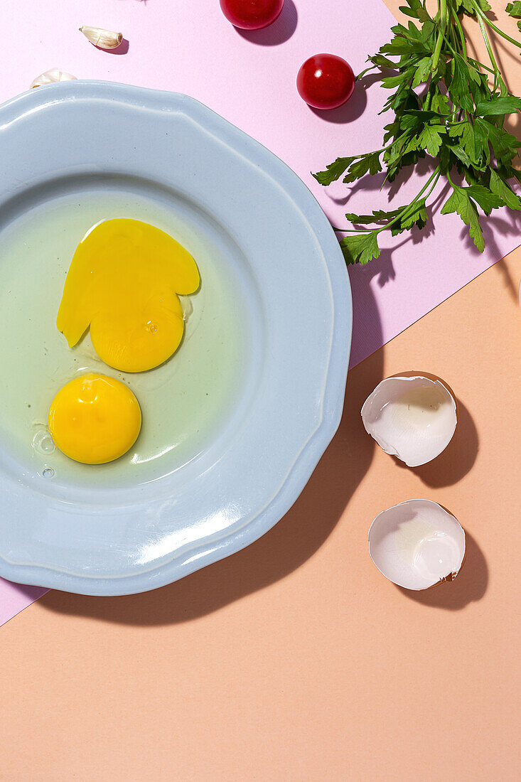 Draufsicht auf rohe Eier auf einem Teller vor Eierschalen und frischen Petersilienzweigen auf zweifarbigem Hintergrund