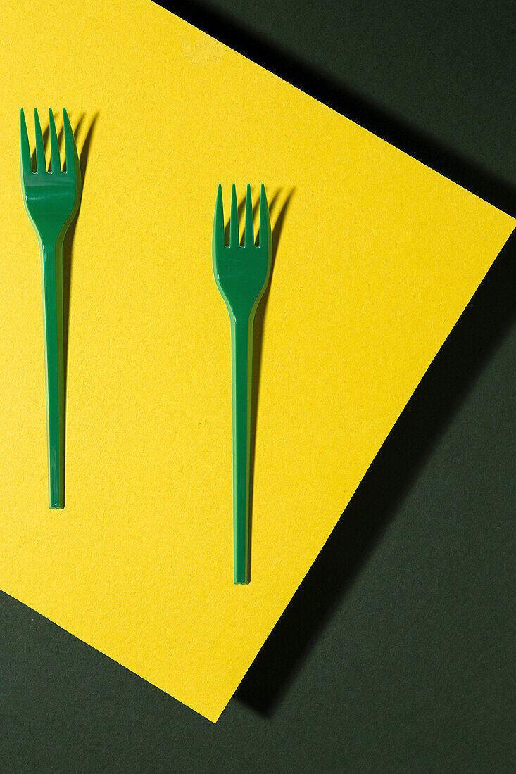 Overhead view of bright green eco friendly fork near yellow carton sheet on green background