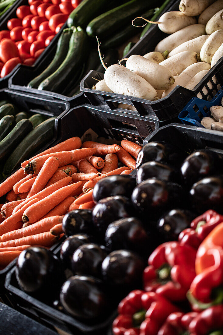 From above of ripe red peppers cucumbers carrots zucchini daikon and mushrooms placed on stall in local market