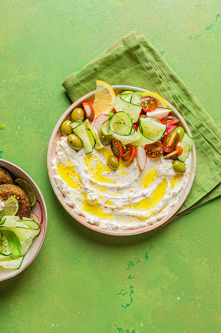 Draufsicht auf einen Teller mit leckerem Frischkäse und verschiedenen Gemüsesorten auf einer Serviette neben veganen Krapfen auf grünem Hintergrund