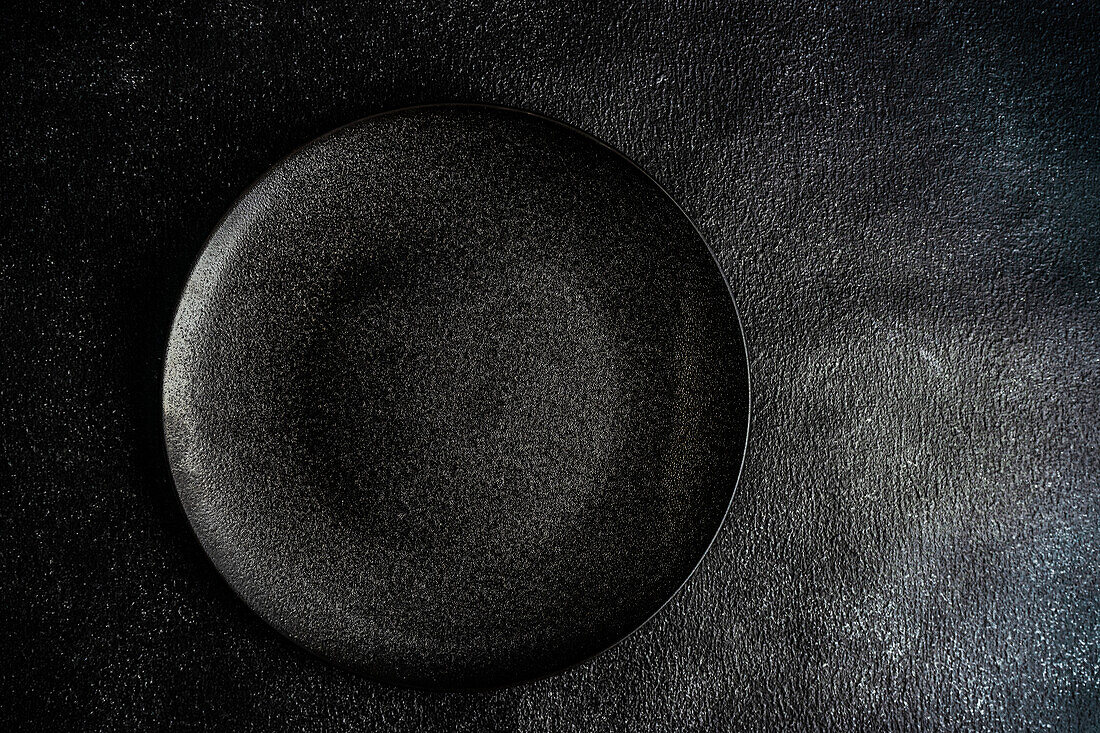 From above minimalistic table setting with black ceramic plate on the same color concrete background