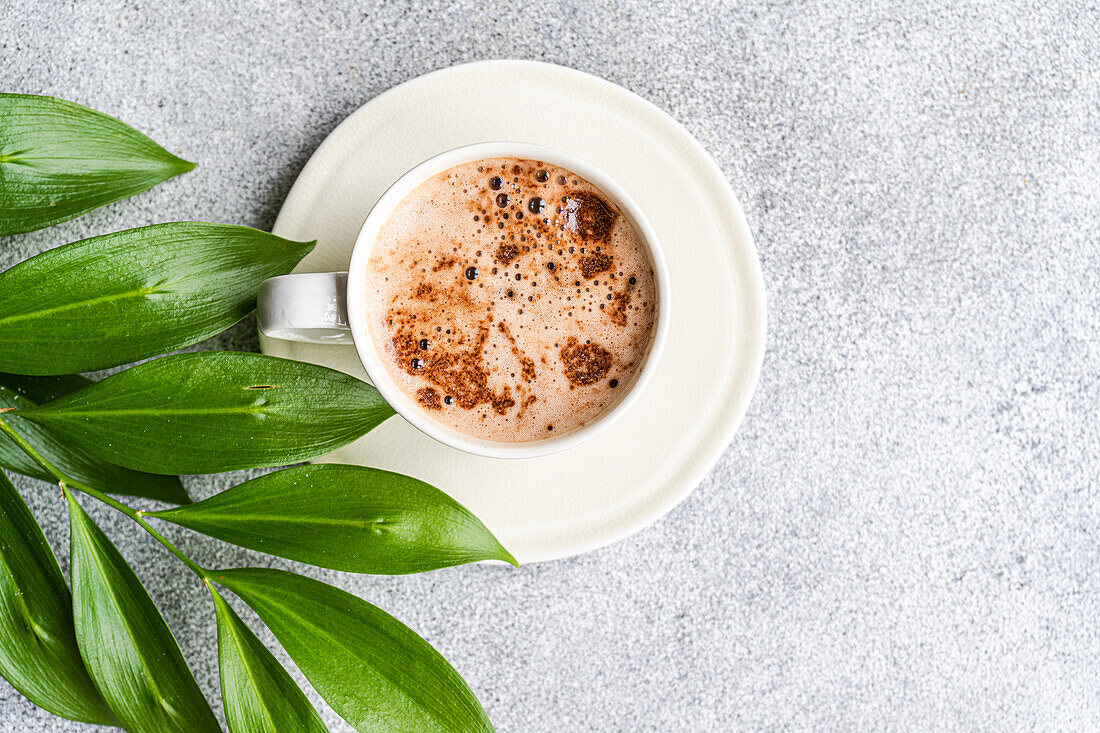 Tasse Cappuccino und grüne Blätter der Ruscus-Pflanze