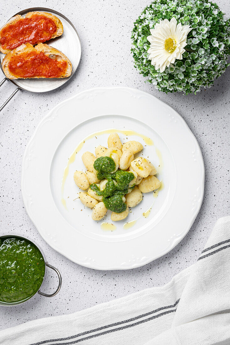 Draufsicht auf appetitliche Gnocchi mit Pesto-Sauce, serviert auf weißem Teller mit Toasts