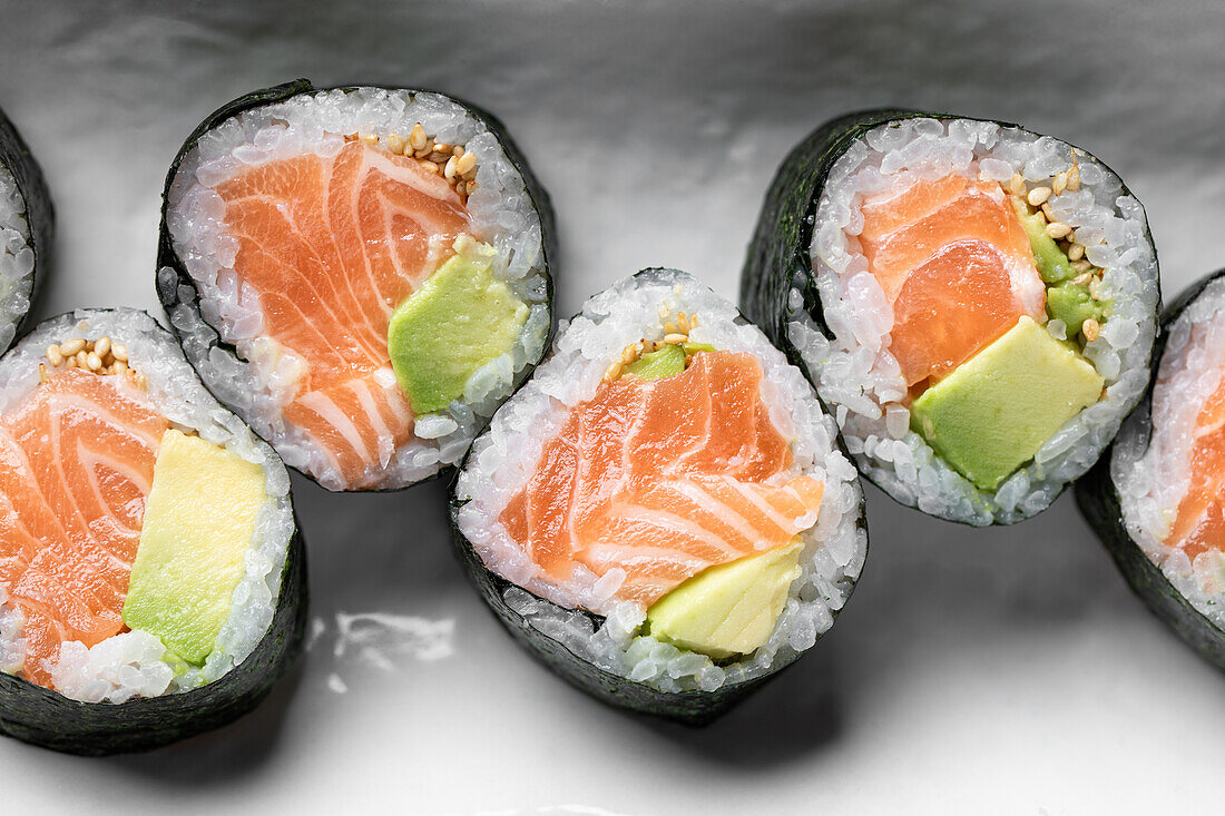 From above set of tasty Futomaki Norwegian sushi rolls with salmon and avocado served on plate in light studio