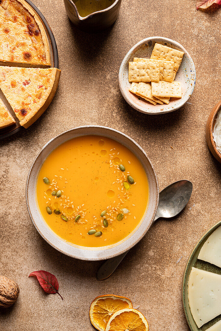 Top view of yummy pumpkin soup with seeds served in bowl near fresh cheese pie and crunchy crackers during lunch