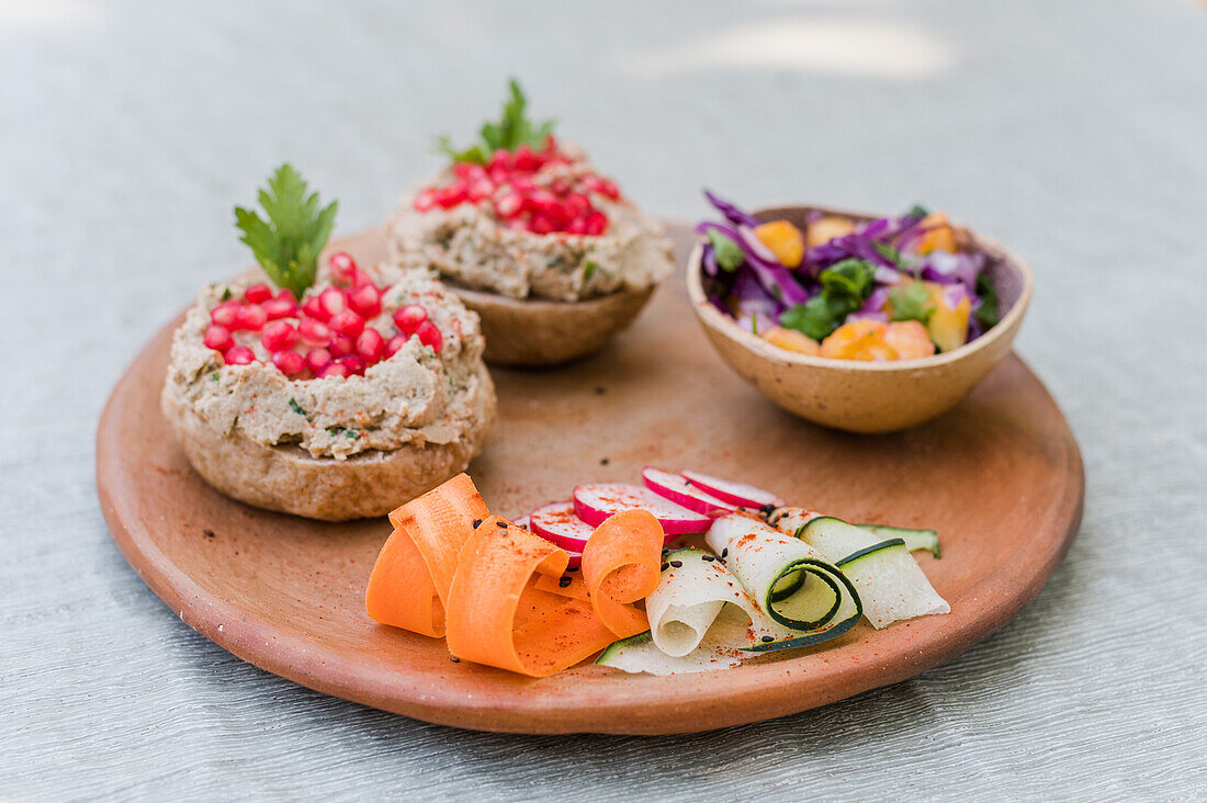 Schüssel mit frischem Salat auf Holzteller mit geschnittenem Gemüse und belegten Brötchen mit Pilzpastete, vorbereitet für ein vegetarisches Mittagessen