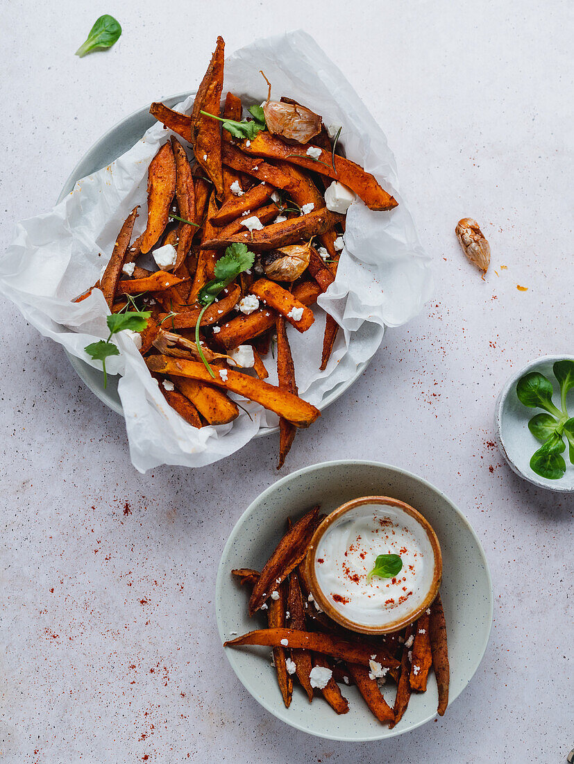 High angle of delicious sweet potato fries with sour cream and herbs served on table