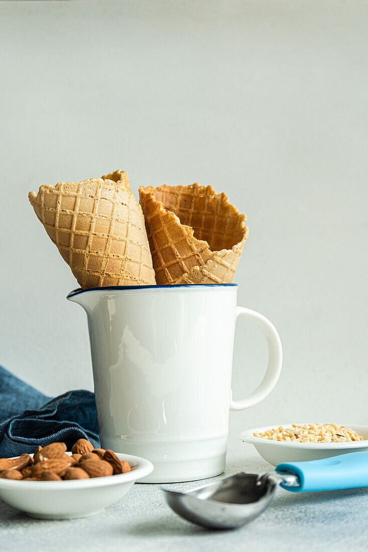 Waffle cones and nuts for ice cream preparation on concrete table with white concrete background with towel