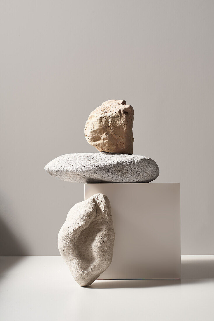Kreative Steine mit unterschiedlichen Formen und Oberflächen auf einem weißen Würfel auf einem Tisch vor weißem Hintergrund in einem modernen hellen Studio