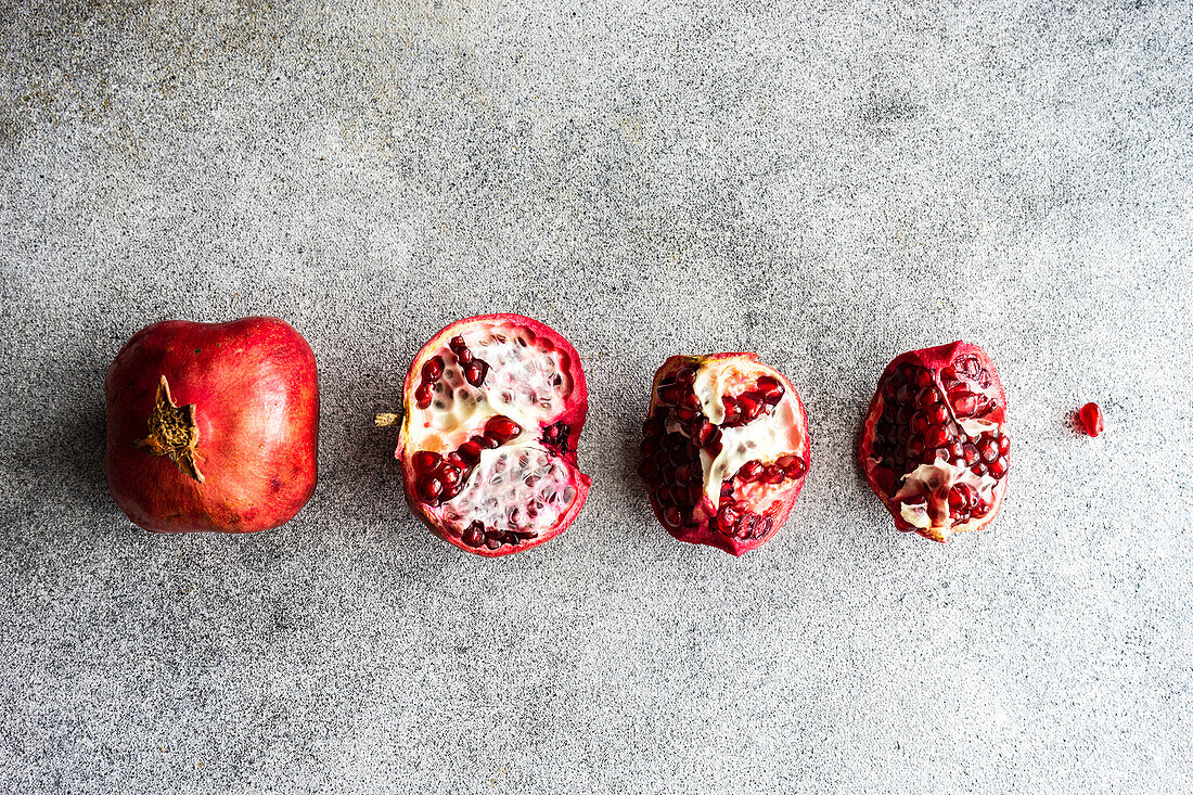 Row of organic ripe pomegranate fruits on grey stone background