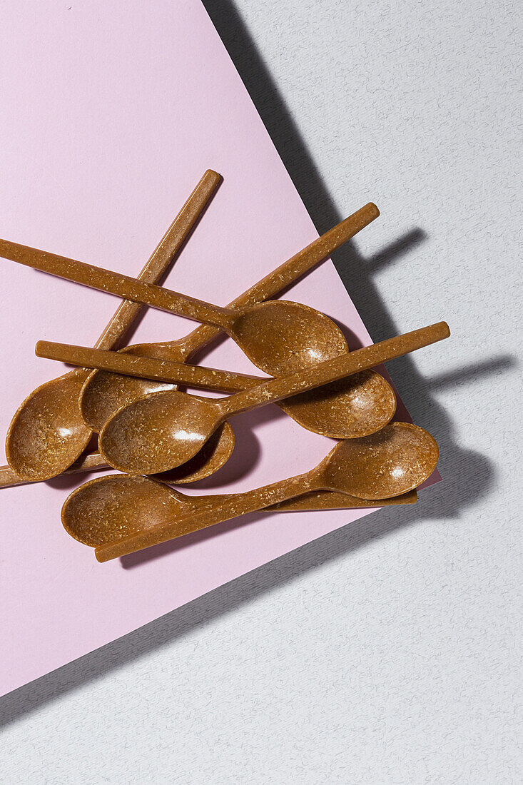 Overhead view of brown eco friendly spoons on pink and white background
