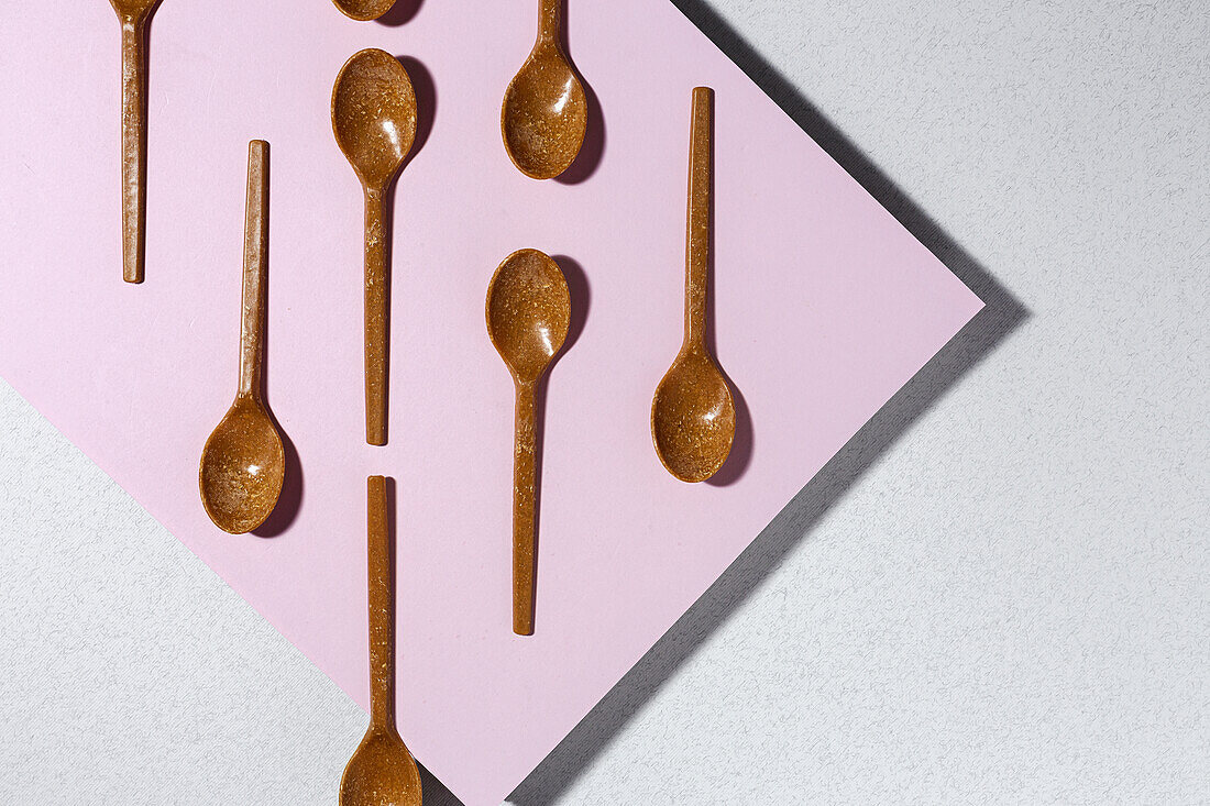 Overhead view of brown eco friendly spoons on pink and white background