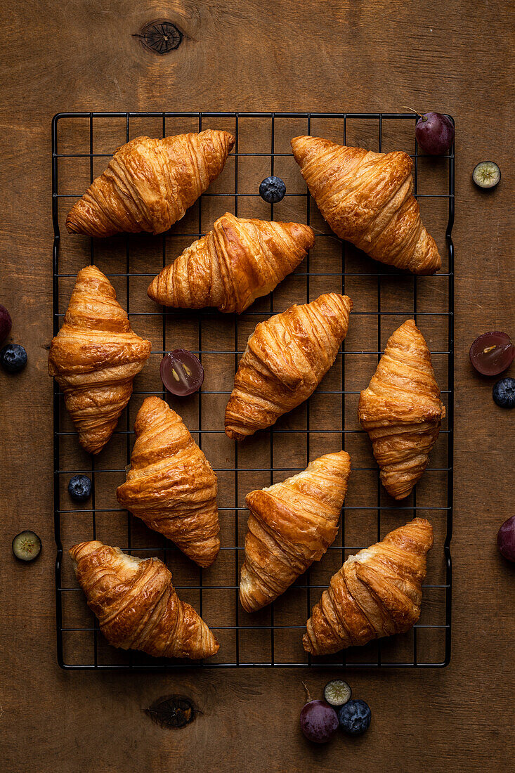 From above tasty sweet fresh baked croissants served with fruits placed on metal grate on wooden table