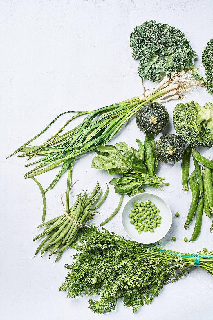 Draufsicht auf verschiedene Bündel grüner Kräuter neben Erbsen in einer Schale und frischem Brokkoli mit Kürbis