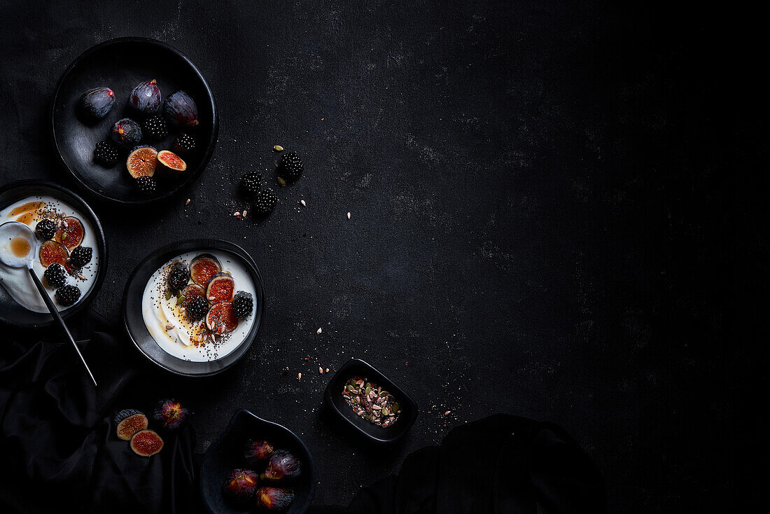 From above of appetizing healthy breakfast consisting of yogurt fresh figs and blackberries sprinkled with seeds and nuts placed on black table