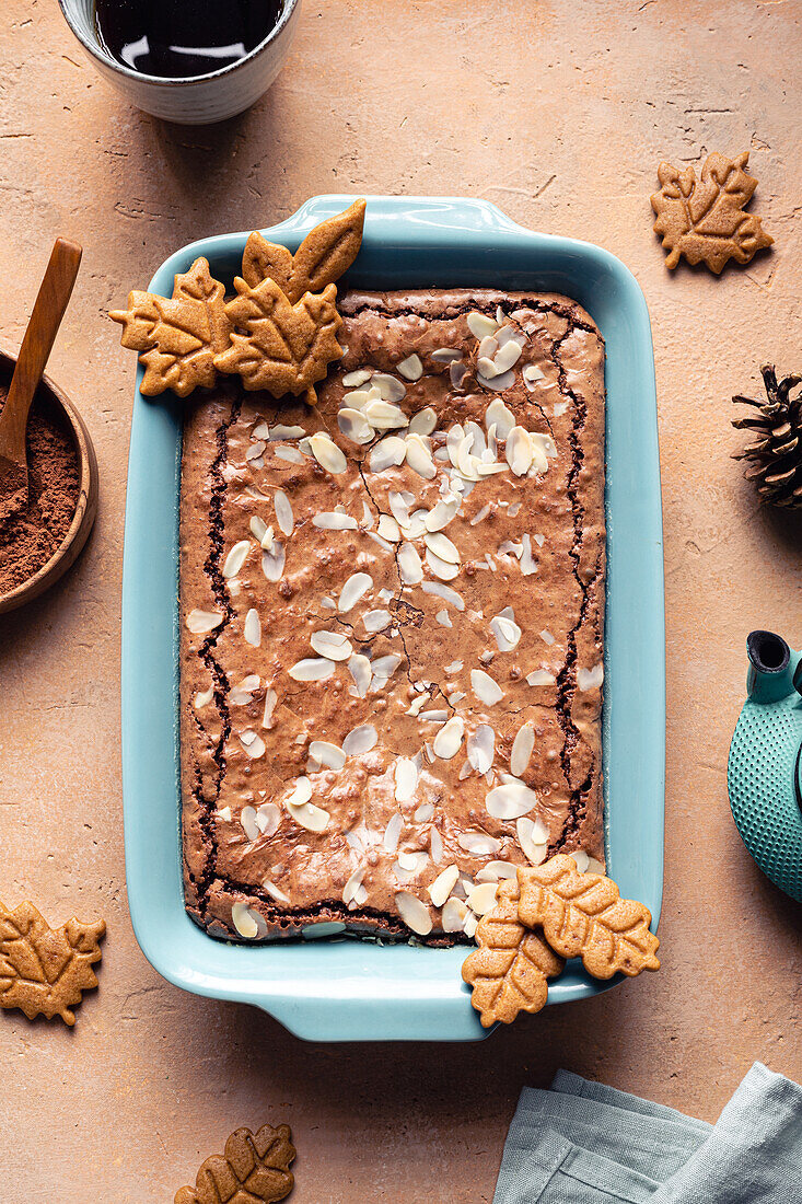 Draufsicht auf leckeren gebackenen Brownie mit Mandelblättchen im Backblech mit Keksen auf dem Tisch mit Kakaopulver