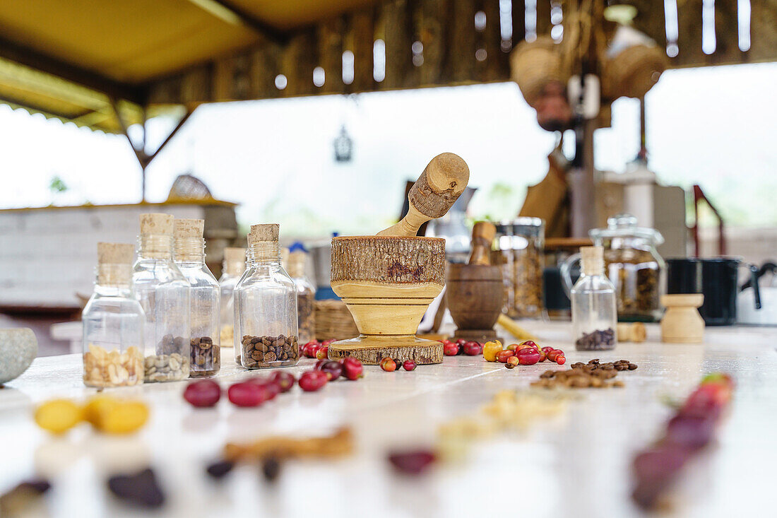 Hölzerne Mörser und Stößel gegen Kaffee Beeren und Bohnen auf dem Tisch auf unscharfen Hintergrund von Steinplatte und Korb platziert