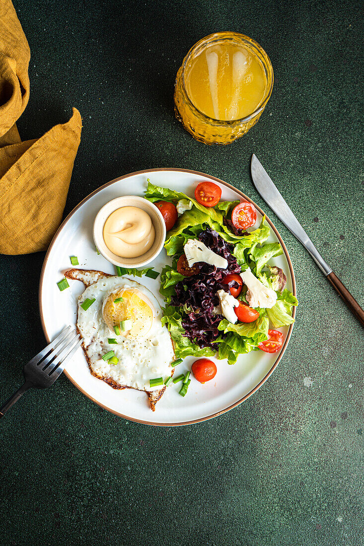 Traditional lunch set with fresh vegetable salad, fried egg and sausages served on green concrete table with glass of fresh made orange juice