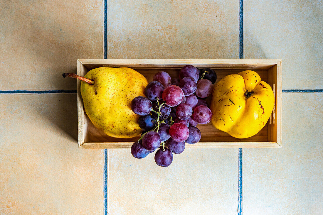 From above box with ripe organic grape, quince and pear on the concrete tiled table