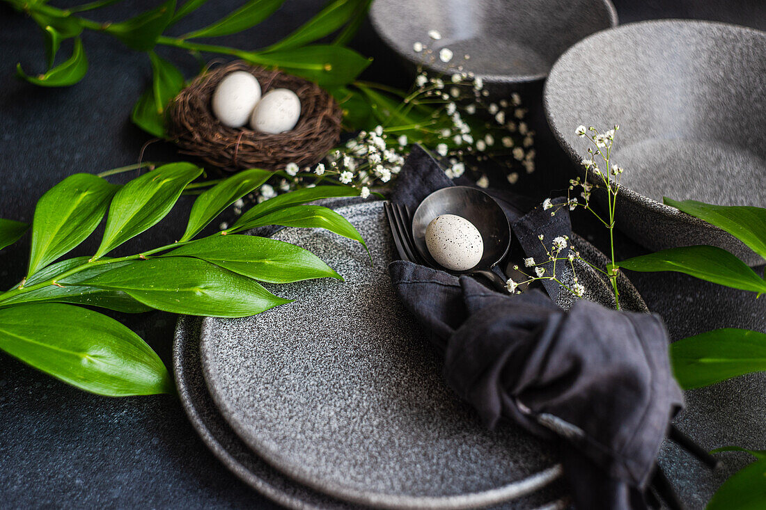 From above place setting for Easter dinner with ceramic plates easter eggs in nest surrounded by Italian ruscus and cushion baby's-breath leaves