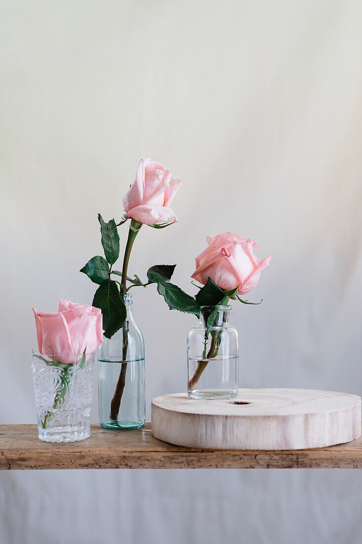 Rosa Rosen in Glasvasen auf einer Holzfläche vor neutralem Hintergrund