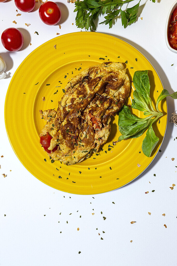 Delicious omelette with chopped parsley on plate against sun dried tomatoes on white background