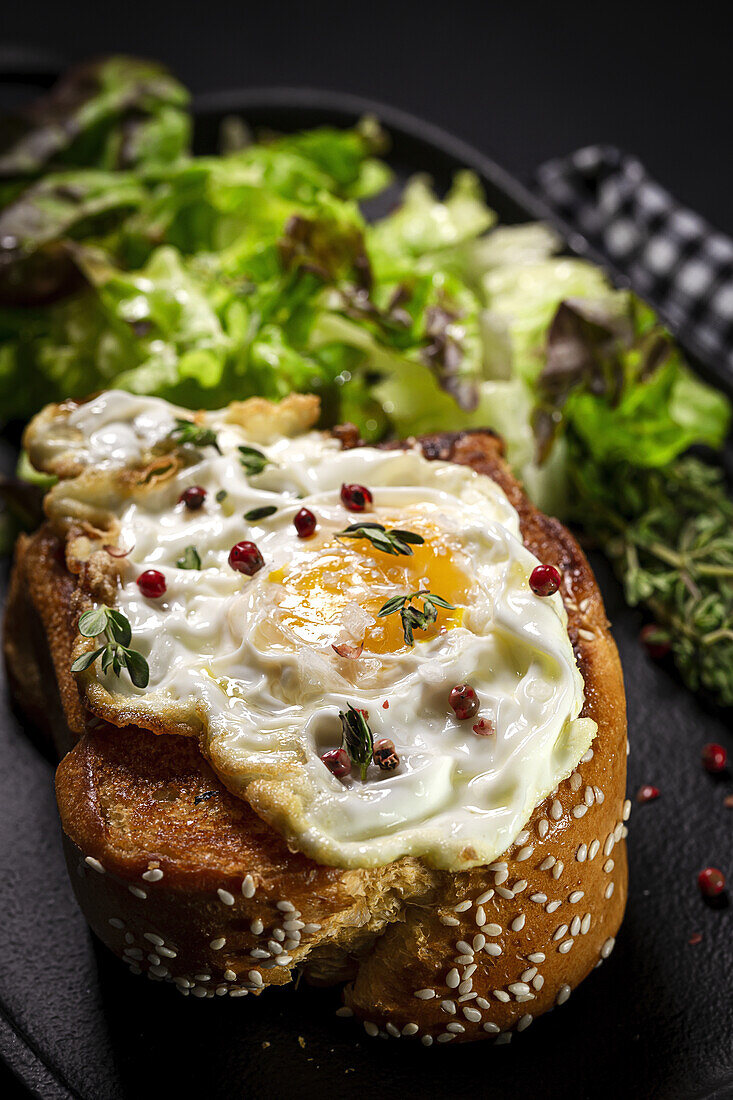 Fried egg on brioche served on tray with fresh lettuce for appetizing breakfast on black background