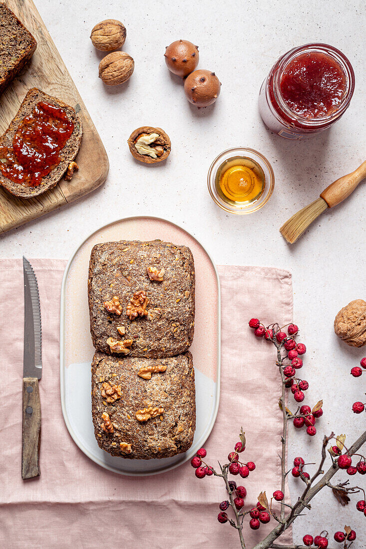 Top view composition of seeded whole grain bread arranged with honey jar of jam and walnut on table near knife
