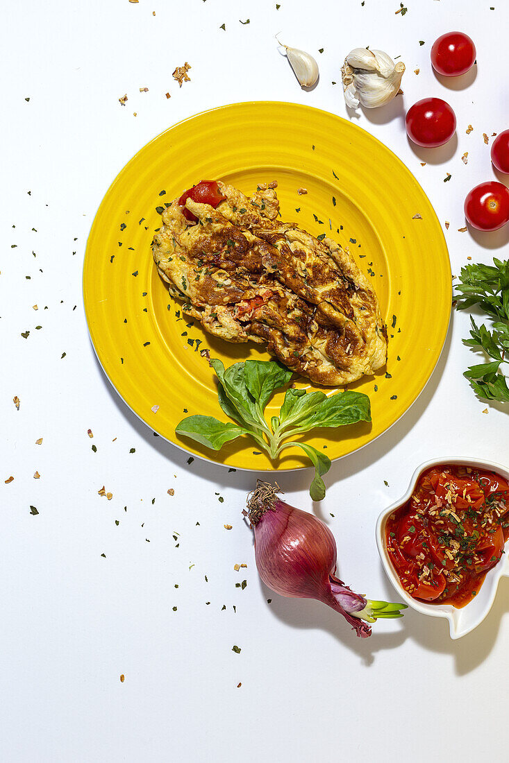 Delicious omelette with chopped parsley on plate against sun dried tomatoes and raw red onion on white background