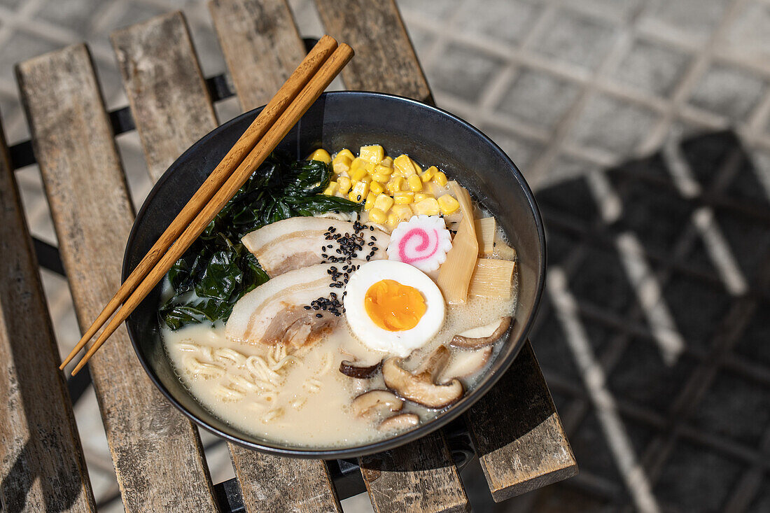 Von oben der appetitlichen japanischen Ramen mit Pilzen und Ei auf Schüssel auf Ecke des Tisches auf der Terrasse des Restaurants auf sonnigen Straße in der Stadt serviert