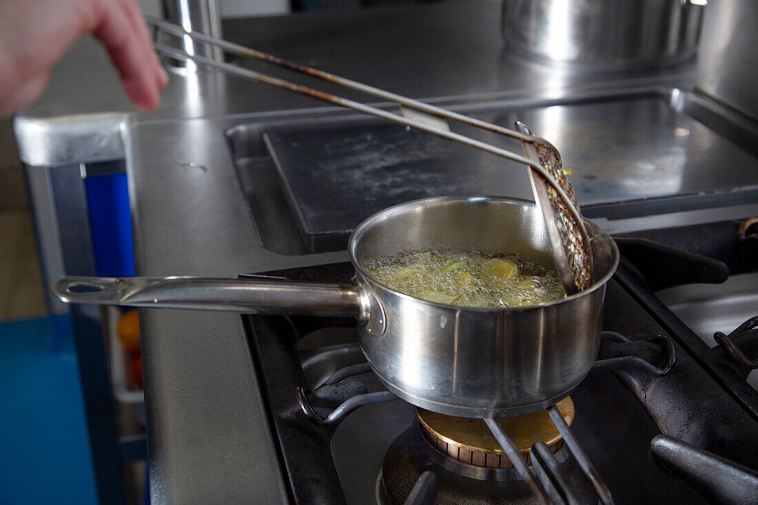 Ausschnitt eines anonymen Kochs, der mit einem Schaumlöffel Krabben in einem Topf mit heißem Öl brät, während er in der Küche eines modernen Restaurants arbeitet