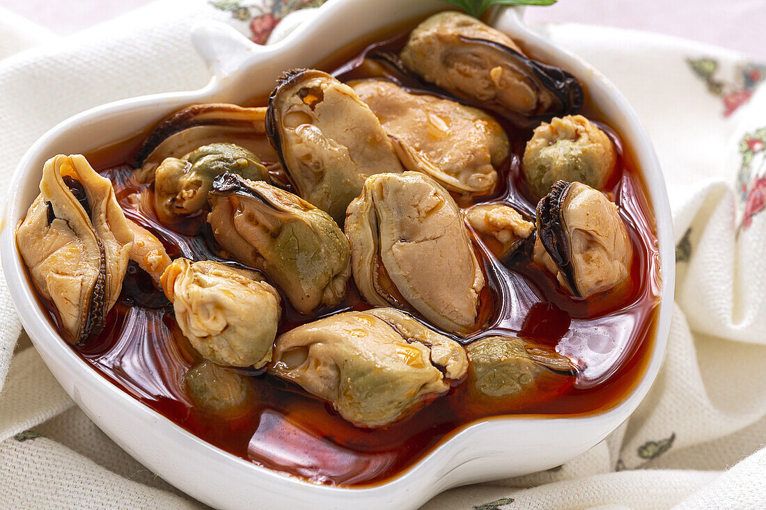 From above ceramic plate with yummy mussels in sauce standing on piece of cloth on gray background