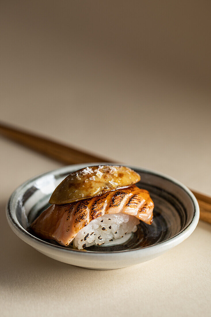 Von oben schmackhafte japanische Nigiri-Sushi mit geräuchertem Lachs und flambierter Gänsestopfleber, serviert auf einem Teller mit Stäbchen in einem Restaurant