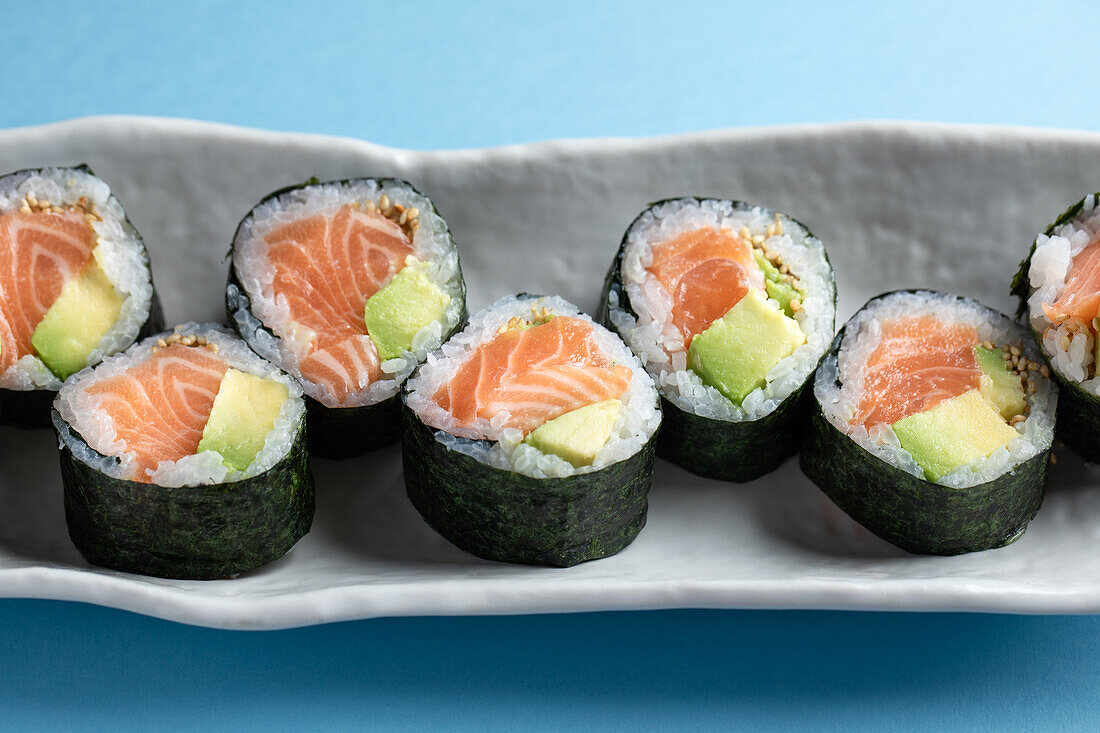 From above set of tasty Futomaki Norwegian sushi rolls with salmon and avocado served on blue background in light studio