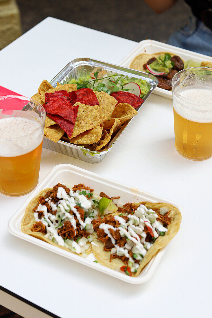 Blick von oben auf appetitliche Nachos mit Salat und Tacos mit Soße auf Tellern mit Biergläsern in einem Restaurant