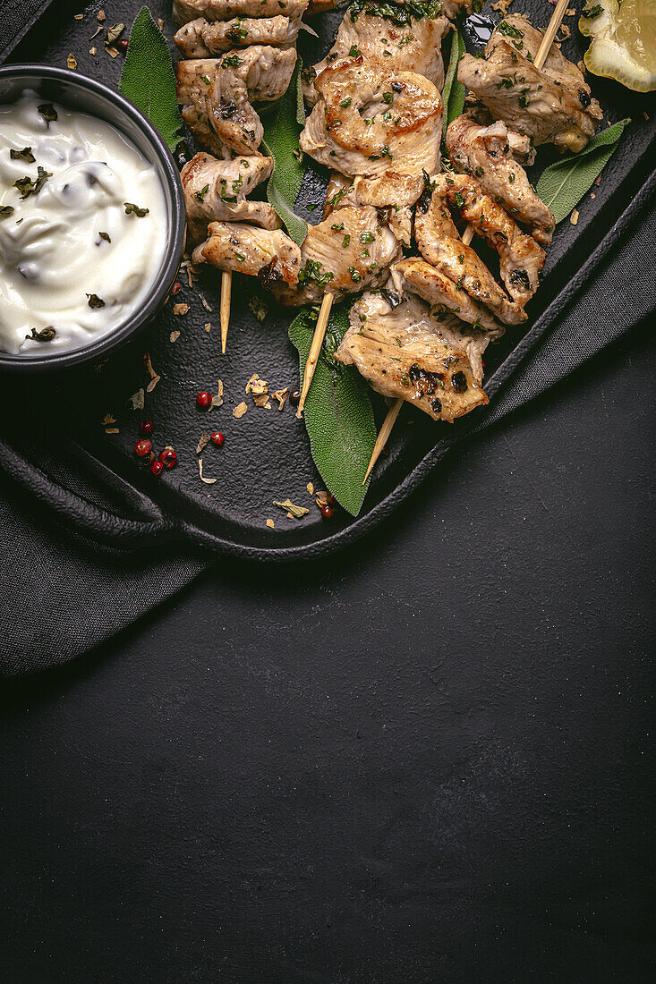 Appetitliches, frisch zubereitetes Fleisch am Spieß, serviert auf einem Tablett auf einem schwarzen Tisch mit einer Schale mit Soße