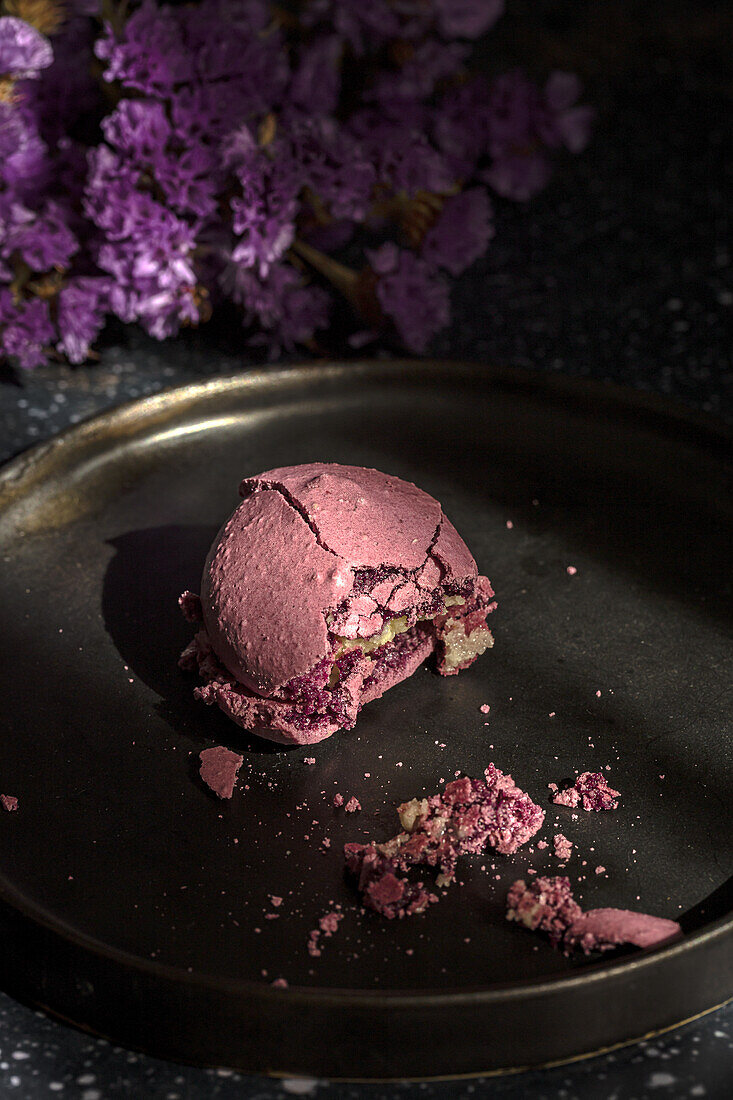 From above bouquet of fresh violet flowers placed on marble table near plate with crushed macaroon in morning.