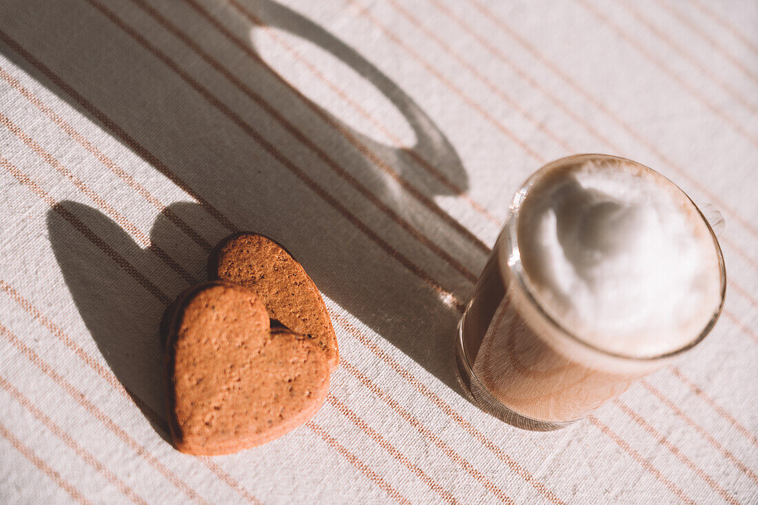 From above glass of foamy latte macchiato served on table with heart shaped cookies on sunny day in kitchen